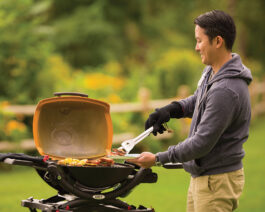 Q 1200 Gas Grill - Orange with a man grilling on it.